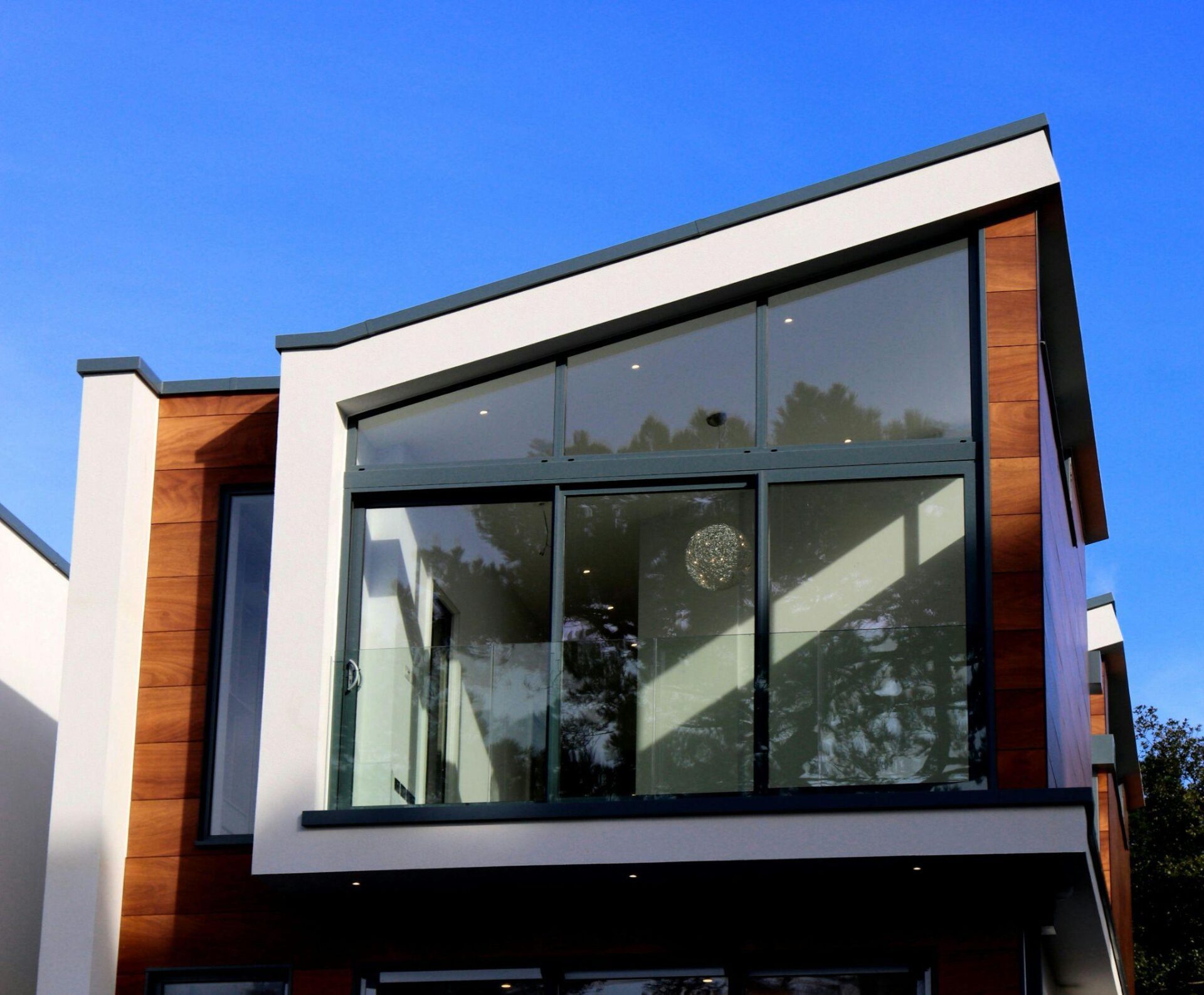 Modern home exterior with large custom glass windows reflecting the sky